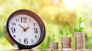 Reloj y pilas de monedas con plantas, como ilustración del ahorro en el tiempo